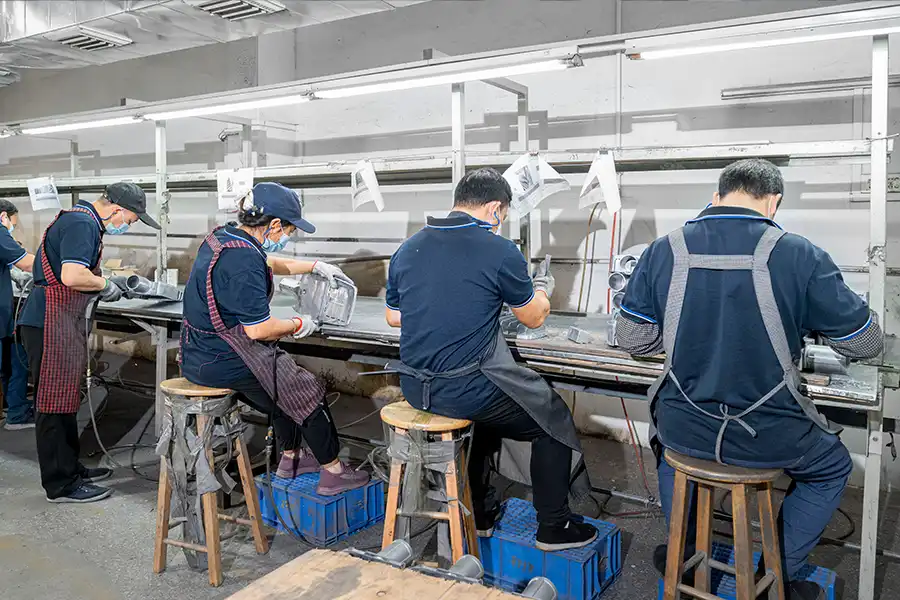 Operators deburring and finishing die cast metal parts at a workshop bench line