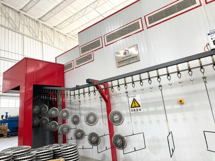 Die cast parts racked on a conveyor entering a coating and curing booth on a finishing line